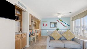 A living room with a sofa, a dining area with chairs, a ceiling fan, and a window with blinds. - Oceanfront North Myrtle Beach Condo | Balcony, Pool, Beach Access & WiFi (North Myrtle Beach)