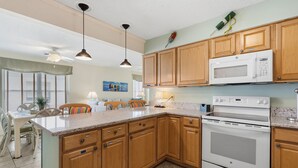 A kitchen with wooden cabinets, a microwave, an oven, and a dining area with chairs and a table. - Oceanfront North Myrtle Beach Condo | Balcony, Pool, Beach Access & WiFi (North Myrtle Beach)
