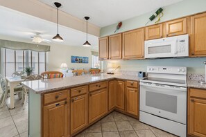A kitchen with wooden cabinets, a microwave, an oven, and a dining area with chairs and a table. - Oceanfront North Myrtle Beach Condo | Balcony, Pool, Beach Access & WiFi (North Myrtle Beach)