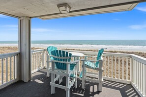 A covered deck with two chairs and a table, overlooking a beach. - Oceanfront North Myrtle Beach Condo | Balcony, Pool, Beach Access & WiFi (North Myrtle Beach)