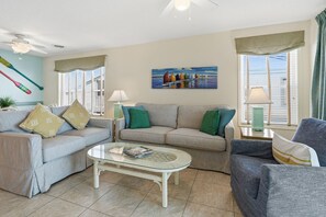 A living room with a sofa, armchair, coffee table, and a painting of sailboats. - Oceanfront North Myrtle Beach Condo | Balcony, Pool, Beach Access & WiFi (North Myrtle Beach)