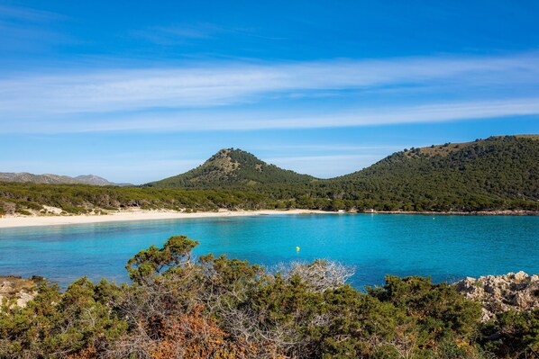 A coastal landscape with a clear blue sea, sandy beach, and green hills. - Vacation Home "Can Nogueras" with Wi-Fi, Balcony, Terrace, Shared Pool and Garden (CALA RATJADA)