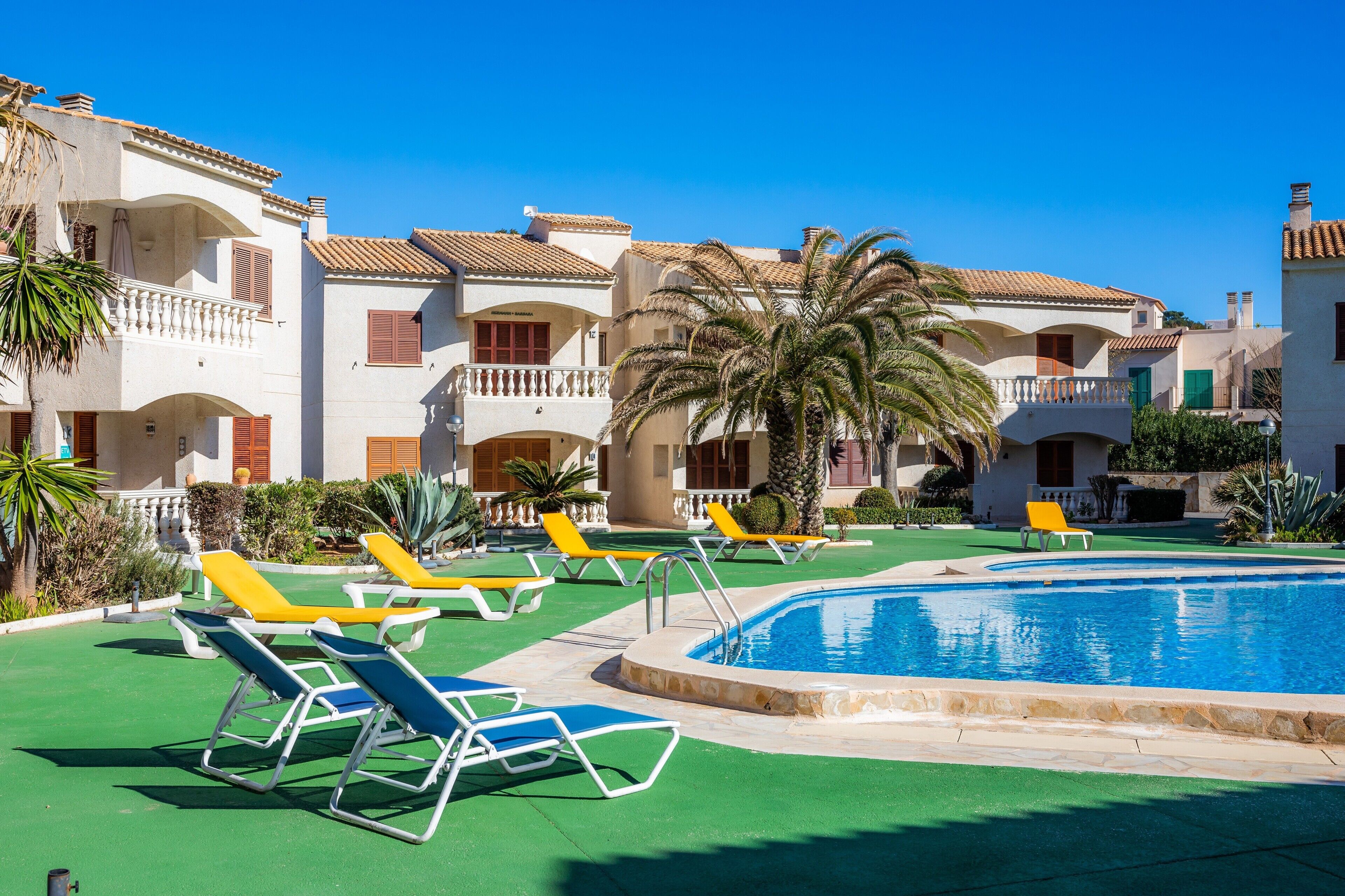 Zona de piscina con sillones, piscina y edificios de varios pisos con balcones.