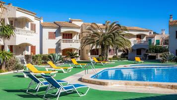 Zona de piscina con sillones, piscina y edificios de varios pisos con balcones.