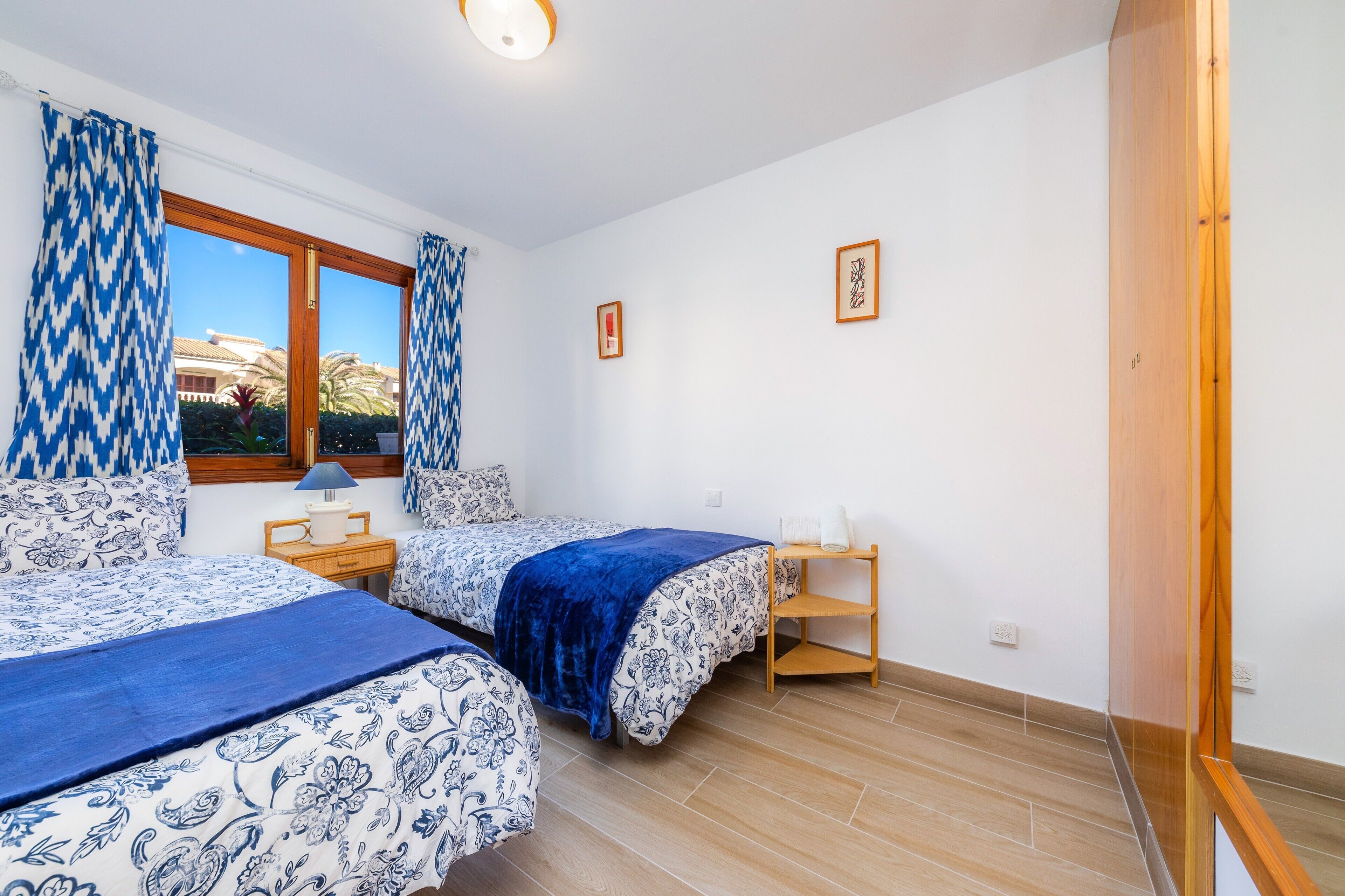 Un dormitorio con dos camas, una ventana con cortinas, una mesita de noche y una estantería.