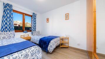 Un dormitorio con dos camas, una ventana con cortinas, una mesita de noche y una estantería.