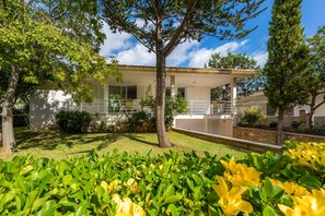 A two-story house with a covered patio, a lawn, and a variety of shrubs and trees. - Near lake, beach and town centre - Casa Can Francesc (Alcudia)