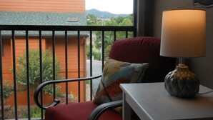 Un balcón con una silla roja, una lámpara y vistas a un edificio rojo y zonas verdes.