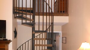 Una escalera de caracol con detalles de madera y barandillas negras, que conduce a un piso superior.