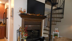 Una sala de estar con chimenea, un televisor encima y una escalera a la derecha.