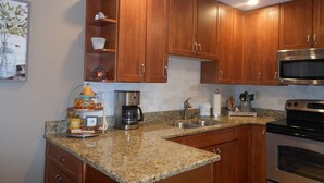 Una cocina con gabinetes de madera, encimeras de granito, microondas de acero inoxidable y cafetera.