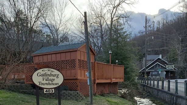 Letrero de Gatlinburg Village Townhouses, con un edificio de madera rústica y un río al fondo.