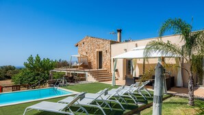 Une piscine avec des chaises longues, un bâtiment en pierre et un ciel dégagé.
