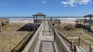 A wooden boardwalk leading to beach huts with a view of the ocean. - Oceanfront, new floors, beautiful decor, sunrise view from all decks (North Topsail Beach)