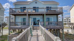A two-story beachfront house with a balcony on each floor, a covered front porch, and a wooden deck leading to the entrance. - Oceanfront, new floors, beautiful decor, sunrise view from all decks (North Topsail Beach)