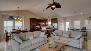 A spacious living room with two sofas, a coffee table, and a dining area with a chandelier. - Oceanfront, new floors, beautiful decor, sunrise view from all decks (North Topsail Beach)