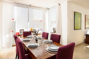 A dining area with a wooden table set for four, purple chairs, and a view through a glass door.