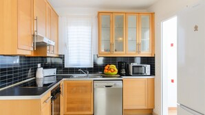 Une cuisine moderne avec des meubles en bois, un lave-vaisselle, un four à micro-ondes et un panier à fruits posé sur le plan de travail.