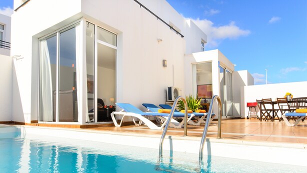 Une piscine avec des chaises longues et un transat, une entrée avec une porte vitrée et un espace patio comprenant une table et des chaises.