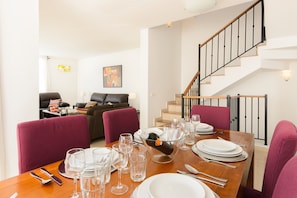 A dining area with a wooden table set for a meal, surrounded by chairs, and a staircase in the background.