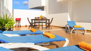 Un espace de détente extérieur, baigné de soleil, avec des fauteuils bleus, une table à manger et une chaise rouge.