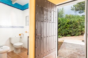 Un baño con inodoro, bidé y lavamanos, y una puerta de madera que da a un espacio exterior.