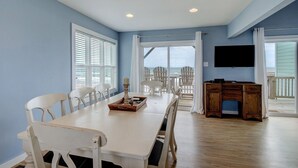 A spacious dining area with a large table, white chairs, and a view of the ocean through large windows. - Direct Oceanfront with 4 Bedrooms, amazing ocean views and beach access- Adjoining side available... (North Topsail Beach)