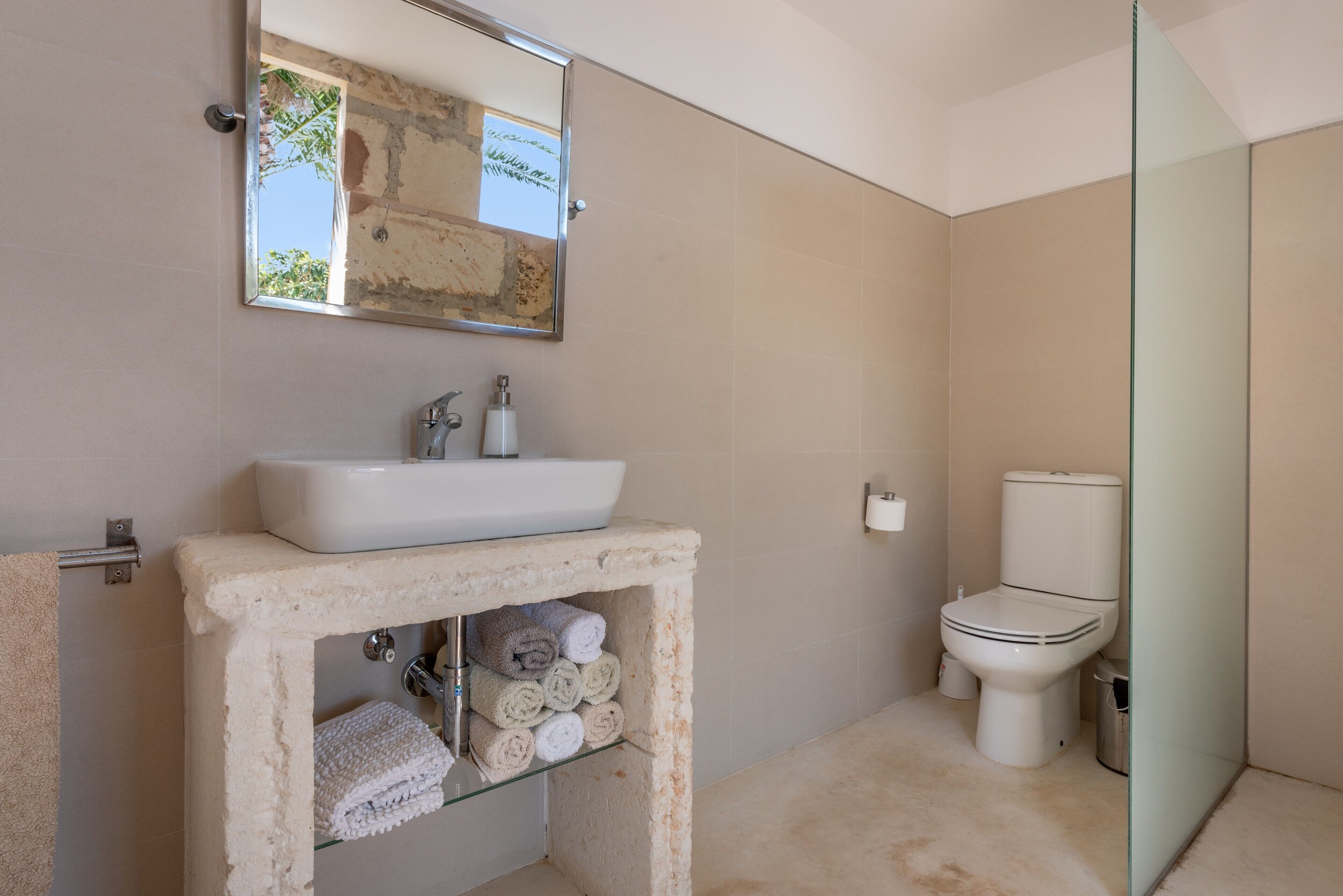 A bathroom with a sink, mirror, toilet, and towel storage.