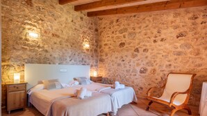 Ein Schlafzimmer mit Steinwänden, zwei Betten, einem Holzstuhl und einem Nachttisch mit Lampe.
