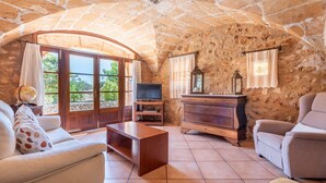 Ein Zimmer mit Steinwänden, das eine Sitzecke mit Sofa und Sesseln, einen Fernseher und große Fenster sowie eine Steindecke bietet.