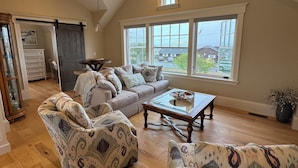 A spacious living room with a high ceiling, large windows, and a cozy seating area with patterned sofas and a wooden coffee table. - Breathtaking views of the Ocean, Incredible Sunrise, Sunsets and Jenness Beach (Rye)
