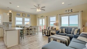 A spacious living area with a large sofa, a dining table, and a kitchen area. - Oceanview Island Retreat with views of The Atlantic and Waterway (North Topsail Beach)