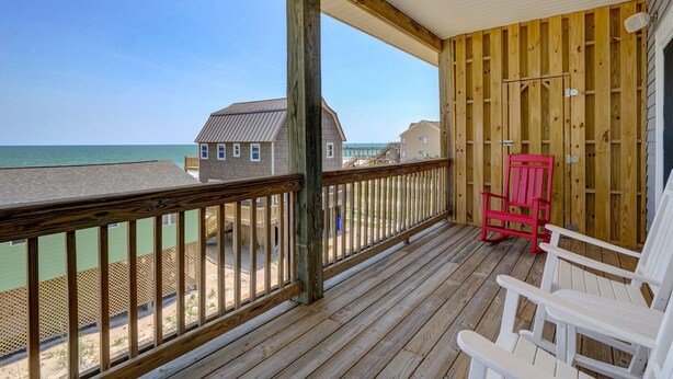 A wooden deck with a railing overlooking a beach, a red chair, and a white chair. - Oceanview Island Retreat with views of The Atlantic and Waterway (North Topsail Beach)