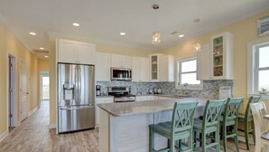 A modern kitchen with white cabinets, stainless steel appliances, and a central island with bar stools. - Oceanview Island Retreat with views of The Atlantic and Waterway (North Topsail Beach)