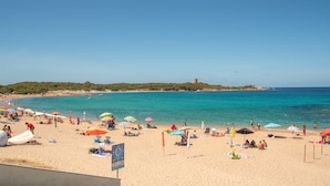 A beach with people sunbathing, umbrellas, and a signboard.