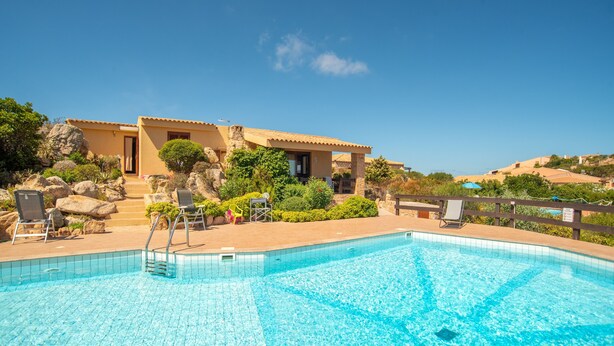A swimming pool with clear blue water, surrounded by a wooden deck with lounge chairs.