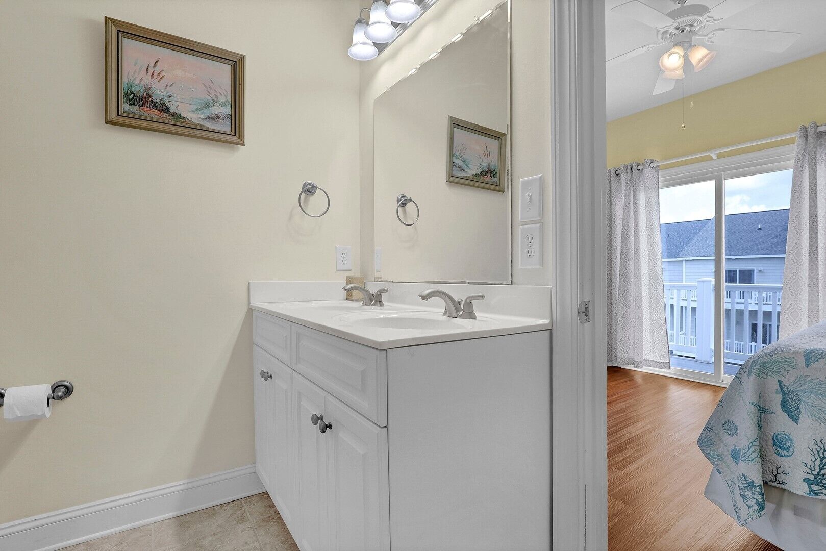 A bathroom with a white vanity, a large mirror, and two framed pictures on the wall.