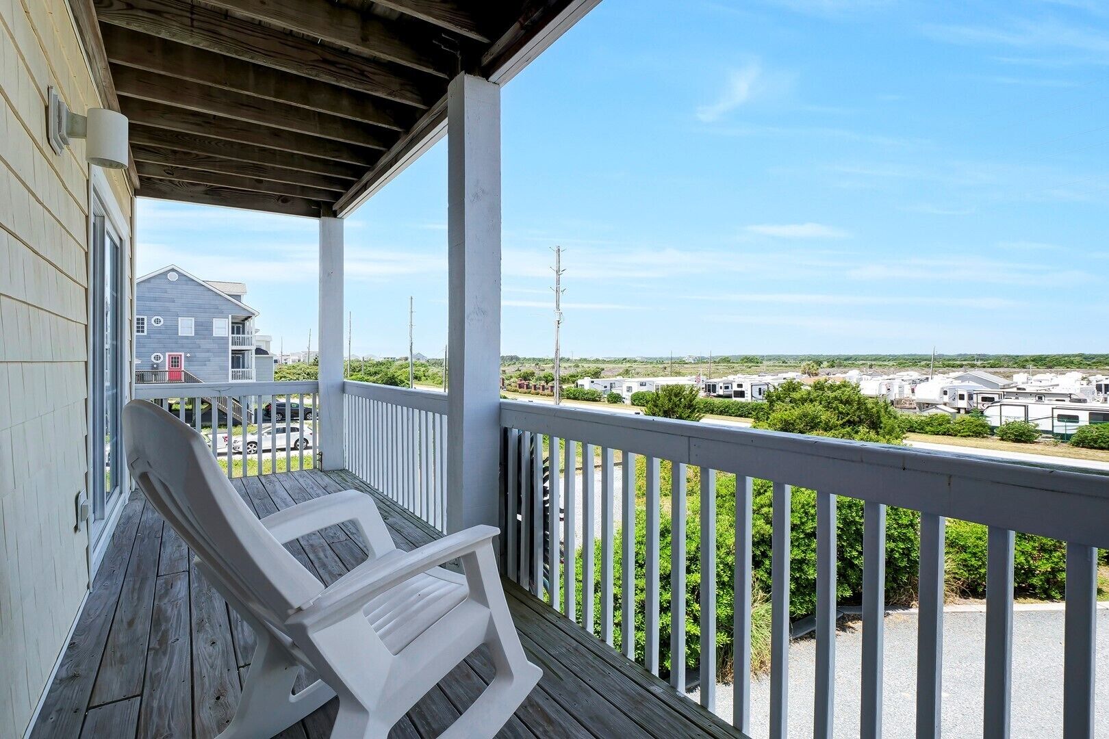 A covered porch with white chairs, a view of a residential area with trailers, and a clear sky.