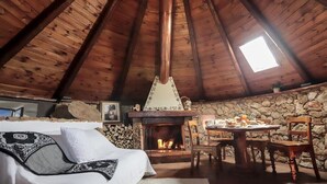 Um quarto de sótão acolhedor com parede de pedra, lareira, mesa de jantar com cadeiras e uma janela grande.