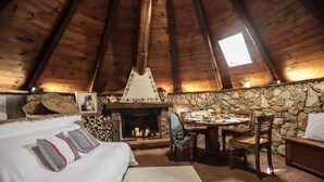 Um quarto de sótão acolhedor com lareira de pedra, vigas de madeira no teto, cama com almofadas e uma mesa de jantar com cadeiras.