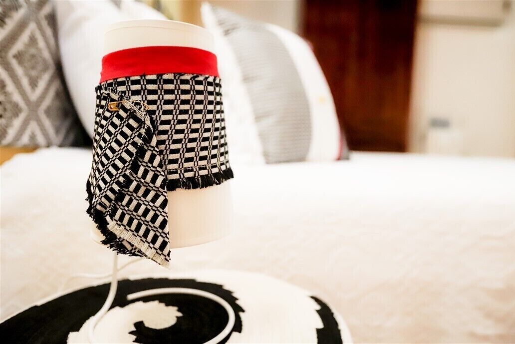 A mug with a checkered pattern and a red band, placed on a bed with a black and white circular design.