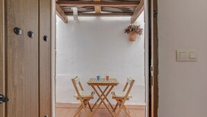 A wooden door with three round handles, a white wall, a tiled floor, a wooden table with two chairs, and a hanging plant. - Enjoy Conil Near the Sea with Pool and Barbecue – Apartment A at Villa Mayo (Conil de la Frontera)