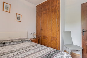 A bedroom with a bed, a wooden wardrobe, a chair, and two framed pictures on the wall. - Enjoy Conil Near the Sea with Pool and Barbecue – Apartment A at Villa Mayo (Conil de la Frontera)