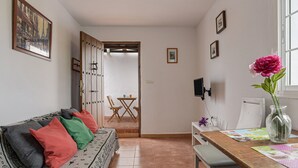 A room with a sofa, a dining table, a vase with flowers, and a door leading to another room. - Enjoy Conil Near the Sea with Pool and Barbecue – Apartment A at Villa Mayo (Conil de la Frontera)