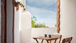 A small patio with a wooden table and chairs, a potted plant, and a clear view of the sky. - Enjoy Conil Near the Sea with Pool and Barbecue – Apartment A at Villa Mayo (Conil de la Frontera)