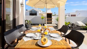 An outdoor dining area with a wooden table, wicker chairs, a large umbrella, and a pizza on the table. - Villa Luna with Mountain View, Pool, Terrace and Wi-Fi (Playa Blanca)