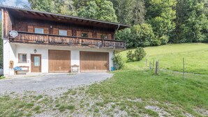 Ein zweistöckiges Holzhaus mit Balkon, zwei Garagentoren und einem Schotterweg.
