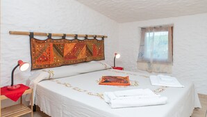 Une chambre à coucher avec un lit, deux lampes de chevet, une fenêtre avec un rideau léger et une tapisserie décorative au-dessus du lit.
