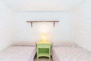 Una habitación pequeña y acogedora con dos camas, una mesita de noche con lámpara y un estante de madera sobre las camas.