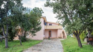 Un chemin de pierres mène à une maison rose, avec une porte et un petit escalier.